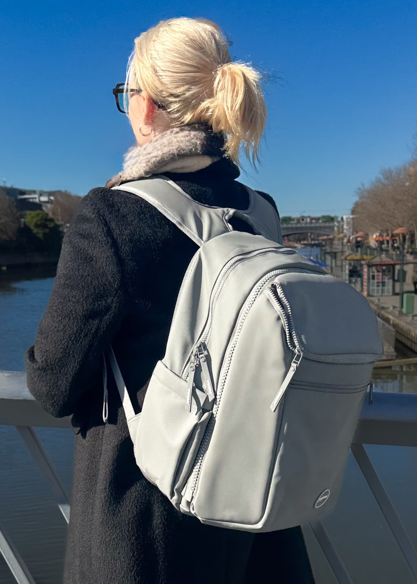 Person with a gray backpack standing on a bridge with a clear blue sky.