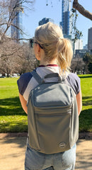Person wearing a grey insulated backpack with the background of a park and city. 