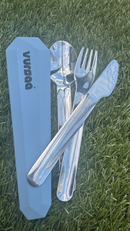 A set of stainless steel fork, knife and spoon with grey and blue toned colored silicone case on grass.