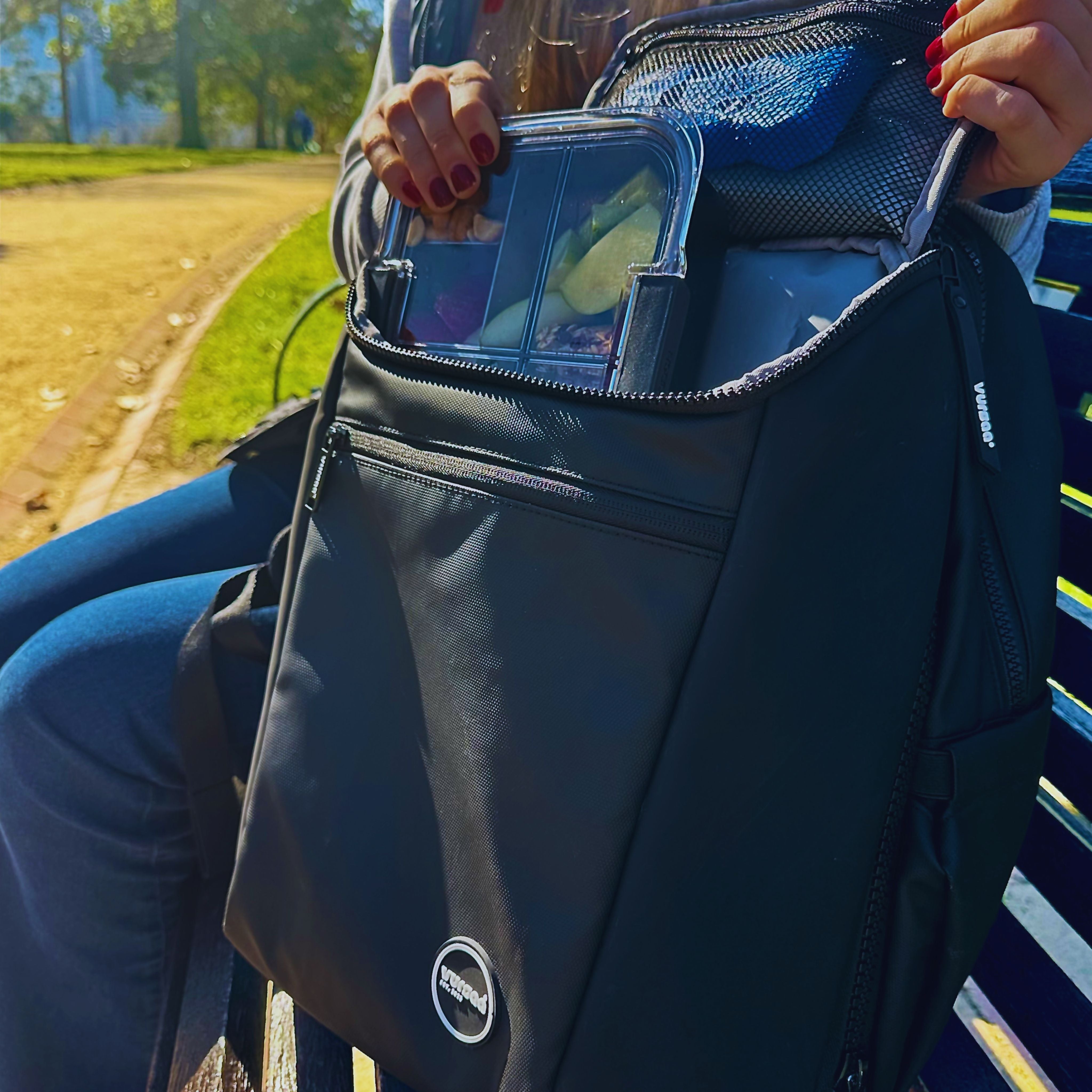 Person holding a black backpack with a visible brand logo, outdoors.