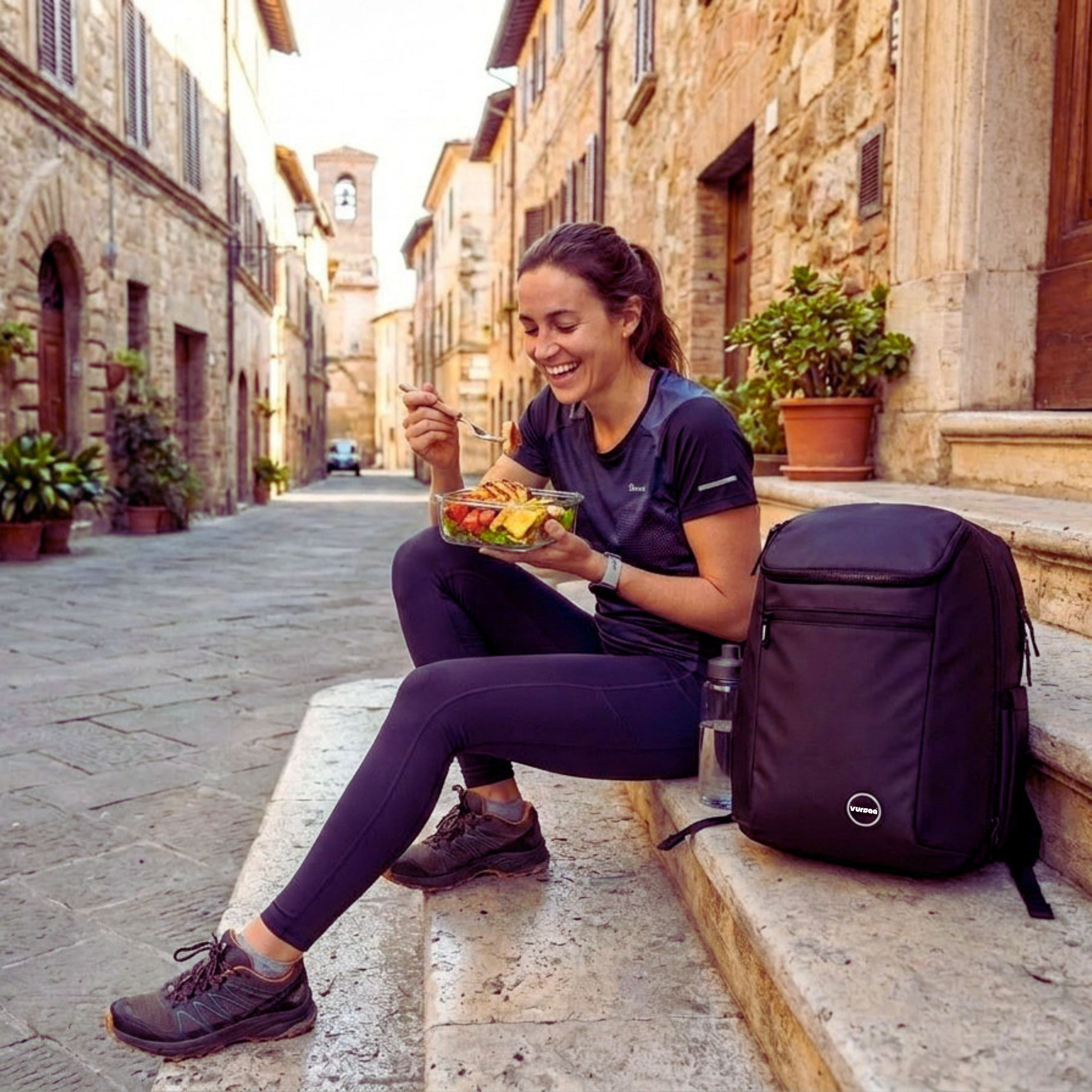 Woman sitting on stone steps eating a salad with a black backpack next to her in an Italian street.