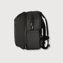 A black backpack shown from the back, featuring multiple zippered compartments, a front pocket, and padded shoulder straps, photographed against a light gray background.
