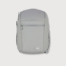 A light gray backpack with a front zippered pocket and a circular logo badge near the bottom, shown against a light gray background.