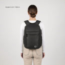 A woman viewed from behind wearing a black backpack on a light gray studio background. Text in the upper left reads 'Model is 5'4" / 163cm'.