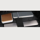 A close-up of a black laptop sleeve or organizer holding multiple tech accessories, including a gold-and-white power bank, a gray notebook secured by a gray elastic band, and a silver laptop.