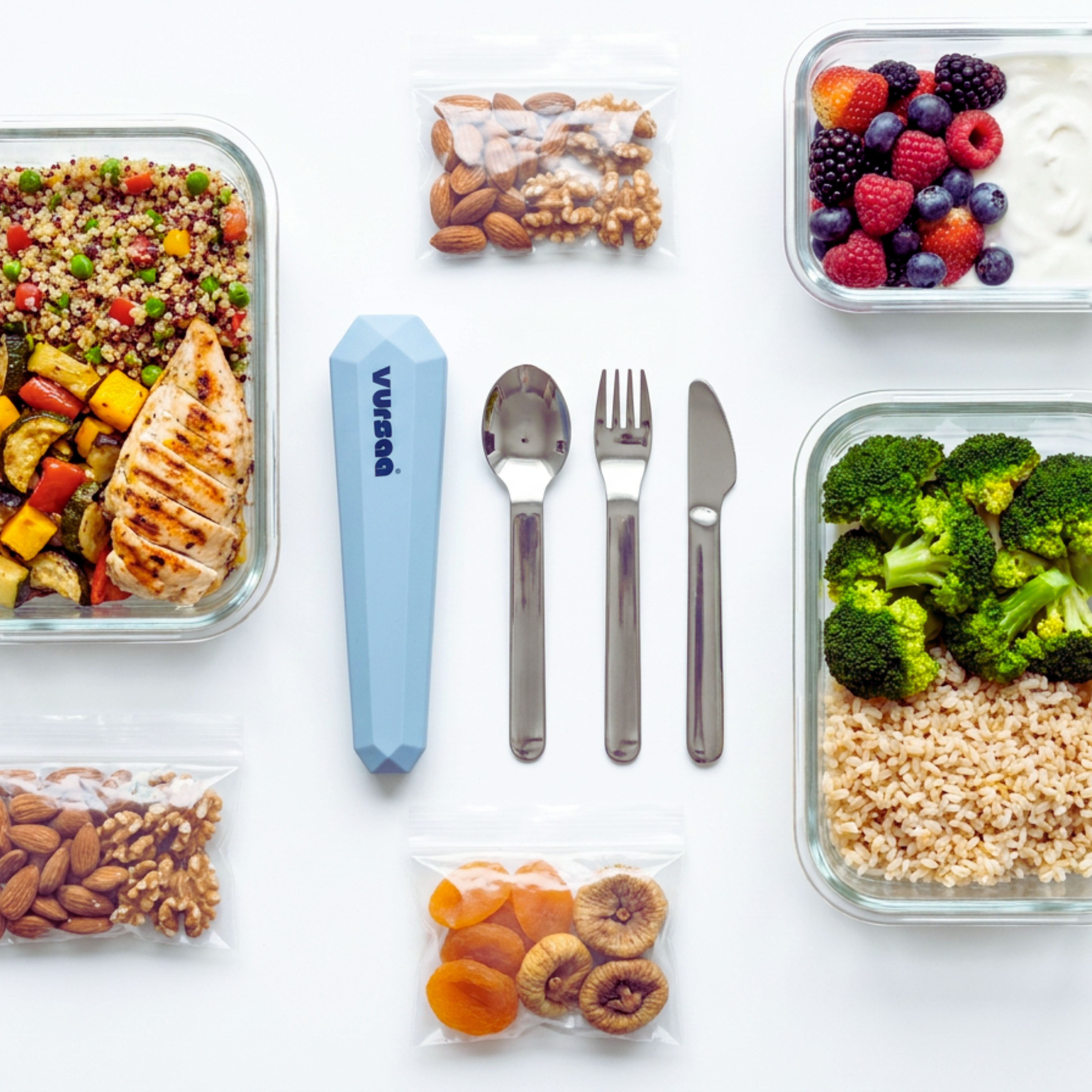 Prepared meals in glass containers with utensils and snacks on a white surface