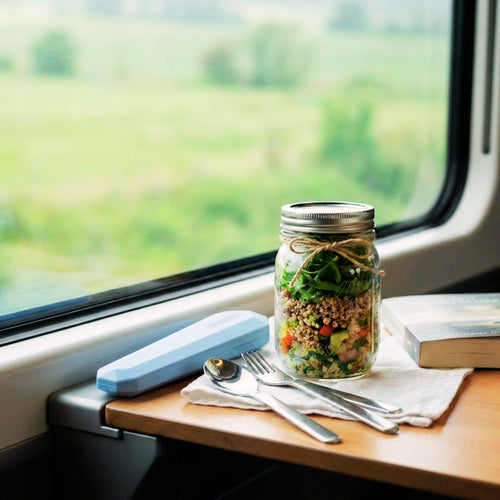Mason jar salad on a train table with a window view and travel utensil